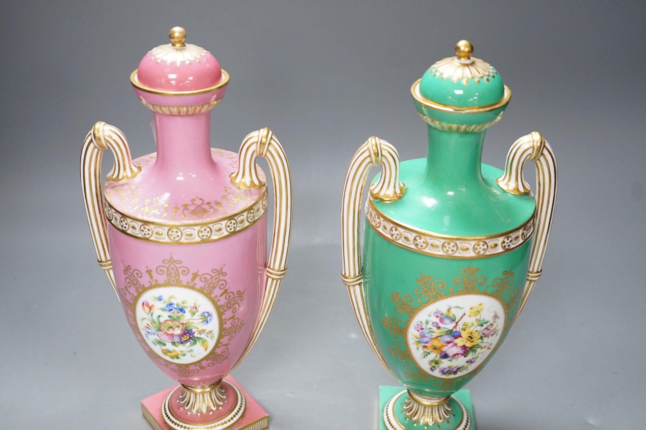 A pair of Coalport Coalbrookdale two handled vases with central oval panelled floral painting and gilt decoration, one green and the other pink, 29cm high